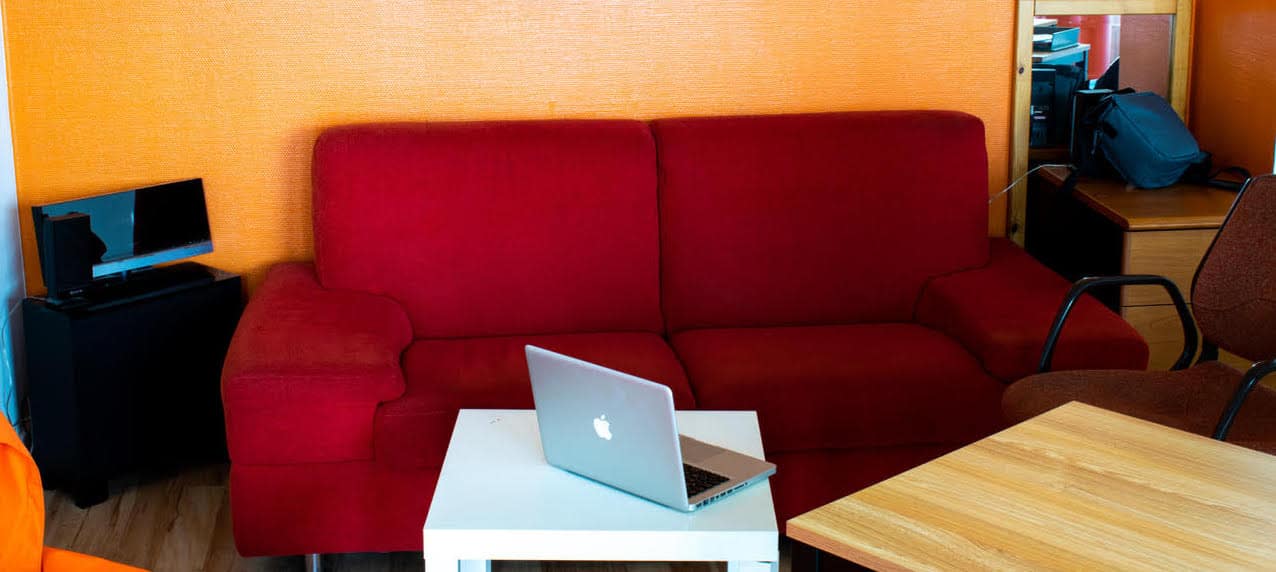 Espace salon, avec canapé rouge et table basse blanche, ordinateur portable mac et mur orange